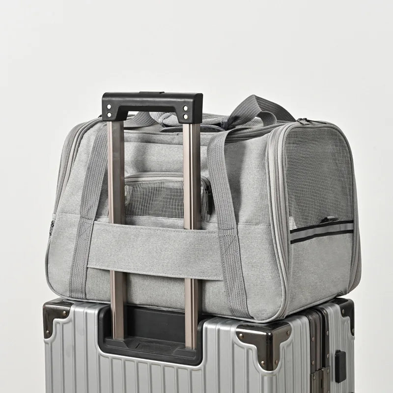 Sac de transport pour chat gris fixé sur la poignée d'une valise trolley grâce à sa sangle arrière dédiée, avec larges fenêtres en maille respirante et bandes réfléchissantes de sécurité.