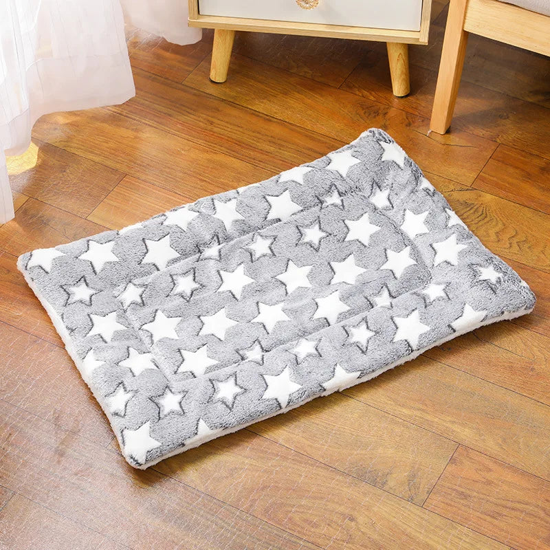 Tapis chat rectangulaire en peluche grise avec grandes étoiles blanches, posé sur un parquet. Ce coussin à chat matelassé offre un confort thermique exceptionnel et une texture douce. Coussin pour chat au design scandinave moderne, idéal comme tapis de sieste chaud. Qualité prestige Les Trésors d'Owka.