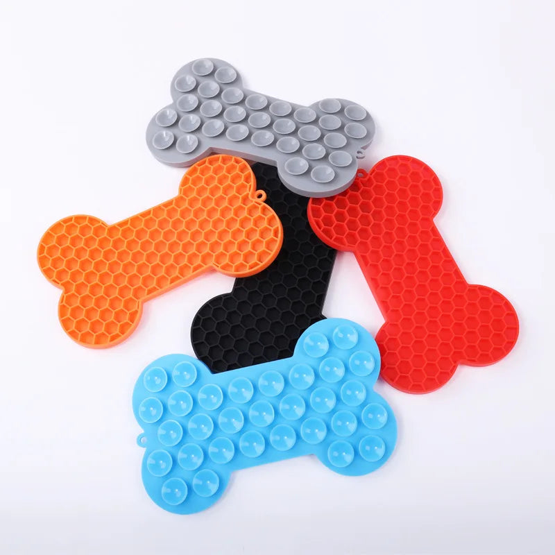 Gamme de tapis de léchage en silicone alimentaire pour chien en forme d'os, montrant la texture nid d'abeille et le système de ventouses de fixation. Ce tapis à lécher anti-anxiété est disponible en bleu, rouge, noir, orange et gris. Un tapis léchage robuste avec ventouses puissantes pour occuper votre animal pendant le bain ou le brossage.