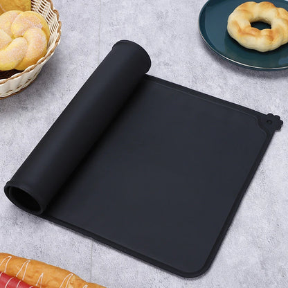 Tapis de gamelle noir en silicone souple partiellement enroulé, imperméable et antidérapant pour chien et chat, avec rebord anti-débordement et motif patte d'animal.