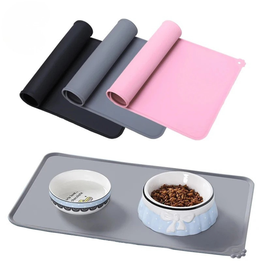 Tapis de gamelle pour chien et chat en silicone souple et imperméable avec bords anti-débordement, disponible en noir, gris et rose, présenté avec une gamelle d'eau et de croquettes.
