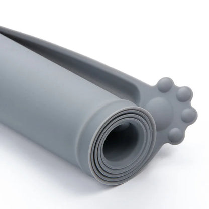 Gros plan d'un tapis de gamelle en silicone gris souple enroulé sur lui-même, montrant sa flexibilité et son design compact avec un motif de patte d'animal pour un rangement facile.