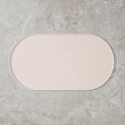 Photographie de face zénithale d'un tapis gamelles chat ovale en silicone blanc crème de la marque Les Trésors d'Owka. Ce tapis chat arbore un design minimaliste avec des bords surélevés anti-débordement pour contenir les projections d'eau et de nourriture, protégeant efficacement vos sols. Fabriqué en silicone alimentaire antidérapant, imperméable et sans BPA, ce tapis gamelles s'intègre parfaitement dans les intérieurs modernes grâce à son coloris ivoire élégant. Sa surface mate et sa facilité de nettoyag