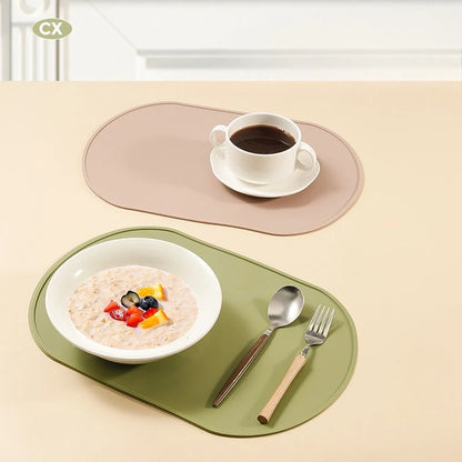 Photographie lifestyle présentant deux tapis gamelles chat ovales en silicone de grade alimentaire dans les coloris vert amande et beige taupe. L'image illustre la polyvalence et la sécurité du produit de la marque Les Trésors d'Owka en y présentant un petit-déjeuner sain, soulignant sa composition sans BPA et sa résistance thermique. Ce tapis chat dispose de rebords surélevés anti-débordement pour contenir efficacement l'eau et la nourriture, offrant une protection optimale pour vos sols et vos tables. Sa 
