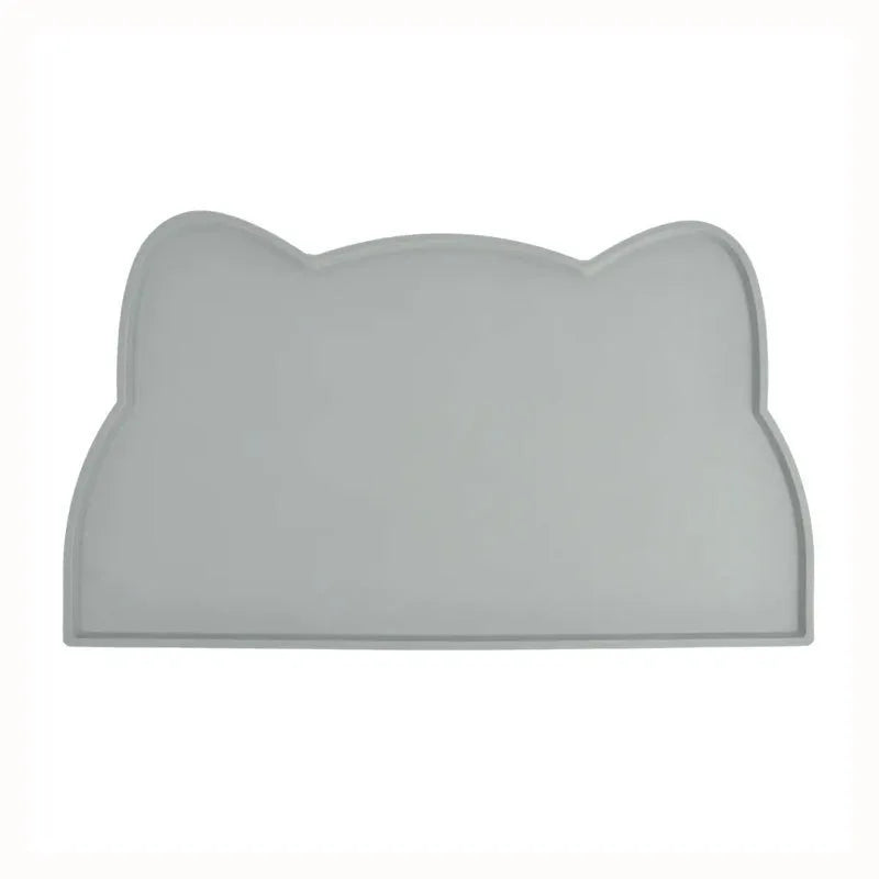 Photographie de face sur fond blanc du tapis gamelles chat en silicone gris de la marque Les Trésors d'Owka. Ce tapis chat arbore un design original en forme de tête de félin avec des bords surélevés anti-débordement pour stopper les projections d'eau et de nourriture. Fabriqué en silicone alimentaire antidérapant et imperméable, ce tapis gamelles offre une protection optimale de vos sols tout en facilitant l'entretien du coin repas. Sa couleur grise sobre et sa finition mate en font l'accessoire d'hygiène 