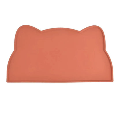 Photographie de face sur fond blanc du tapis gamelles chat en silicone coloris terracotta de la marque Les Trésors d'Owka. Ce tapis chat présente un design original en forme de tête de félin avec des rebords surélevés anti-débordement pour stopper les projections d'eau et de nourriture. Fabriqué en silicone alimentaire antidérapant et imperméable, ce tapis gamelles offre une protection optimale de vos sols tout en apportant une touche décorative chaleureuse à votre intérieur. Sa finition mate et sa couleur 