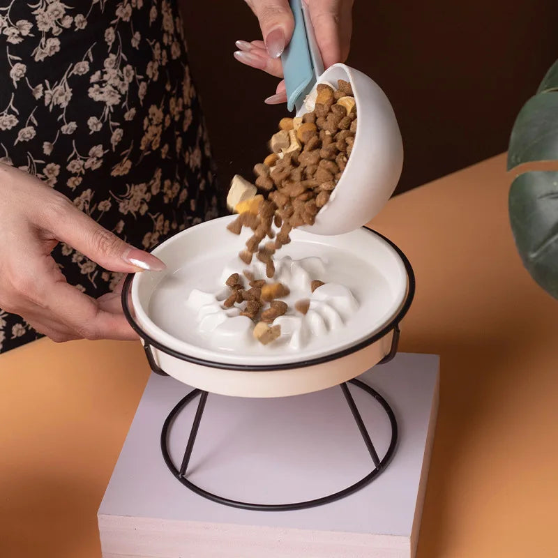 Plan rapproché montrant l'action de verser des croquettes dans une gamelle anti-glouton pour chat en céramique blanche surélevée. Le zoom met en évidence le labyrinthe intérieur en relief, conçu comme un anti glouton chat efficace pour ralentir la prise de nourriture, prévenir les vomissements et améliorer la digestion de votre félin. Solution santé et design disponible chez Les Trésors d'Owka.