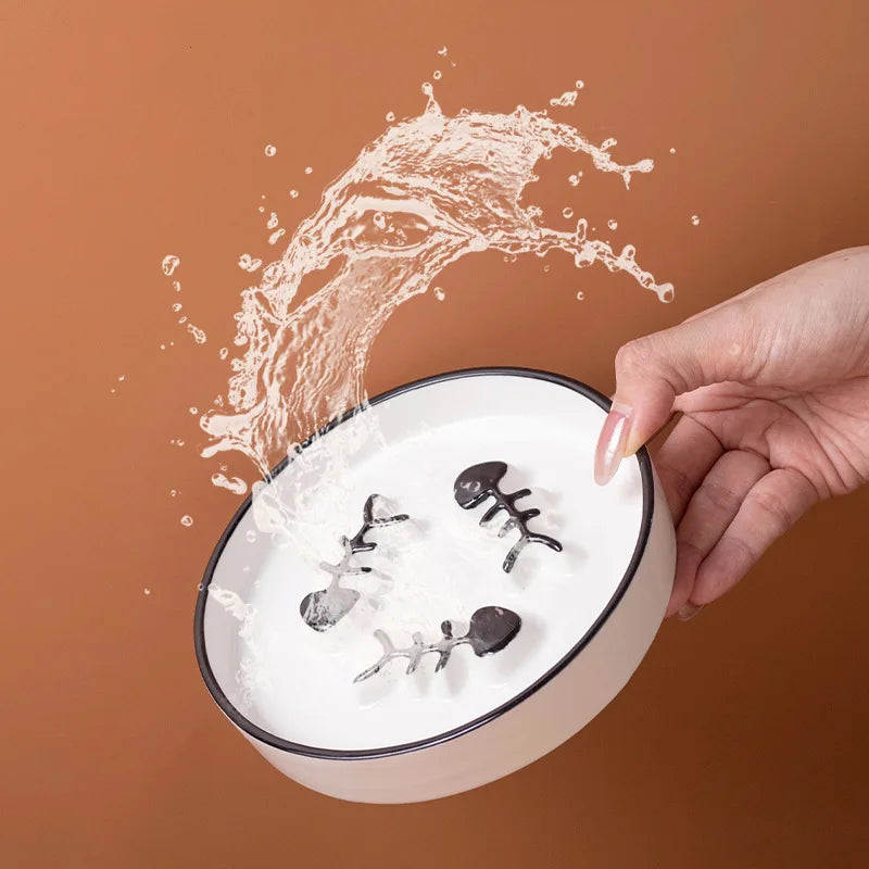 Plan rapproché montrant l'action de verser de l'eau sur une gamelle anti-glouton pour chat en céramique blanche. Le zoom met en évidence le labyrinthe intérieur en relief (arêtes de poisson), conçu comme un anti glouton chat efficace pour ralentir la prise de nourriture et améliorer la digestion. Illustration de la facilité d'entretien du design hygiénique, disponible chez Les Trésors d'Owka.