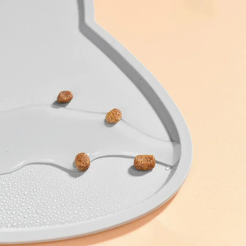 Gros plan détaillé sur le rebord surélevé d'un tapis gamelles chat en silicone gris de la marque Les Trésors d'Owka. L'image illustre parfaitement l'efficacité imperméable du tapis avec des gouttes d'eau et des croquettes contenues sur la surface, protégeant ainsi vos sols des fuites et des saletés. Ce tapis chat haute performance utilise un silicone alimentaire de qualité supérieure pour une hygiène irréprochable du coin repas. Grâce à sa conception anti-débordement, ce tapis gamelles est la solution idéal