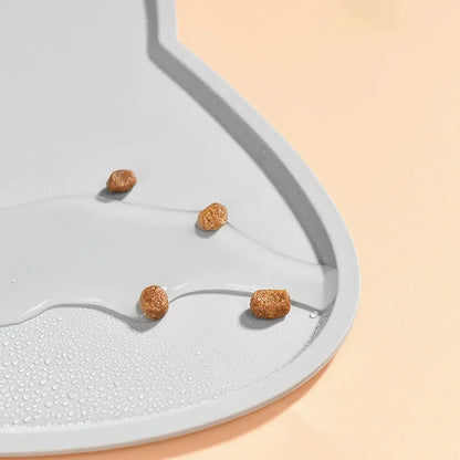 Gros plan détaillé sur le rebord surélevé d'un tapis gamelles chat en silicone gris de la marque Les Trésors d'Owka. L'image illustre parfaitement l'efficacité imperméable du tapis avec des gouttes d'eau et des croquettes contenues sur la surface, protégeant ainsi vos sols des fuites et des saletés. Ce tapis chat haute performance utilise un silicone alimentaire de qualité supérieure pour une hygiène irréprochable du coin repas. Grâce à sa conception anti-débordement, ce tapis gamelles est la solution idéal
